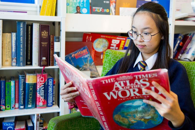 High school student reading an atlas in school library